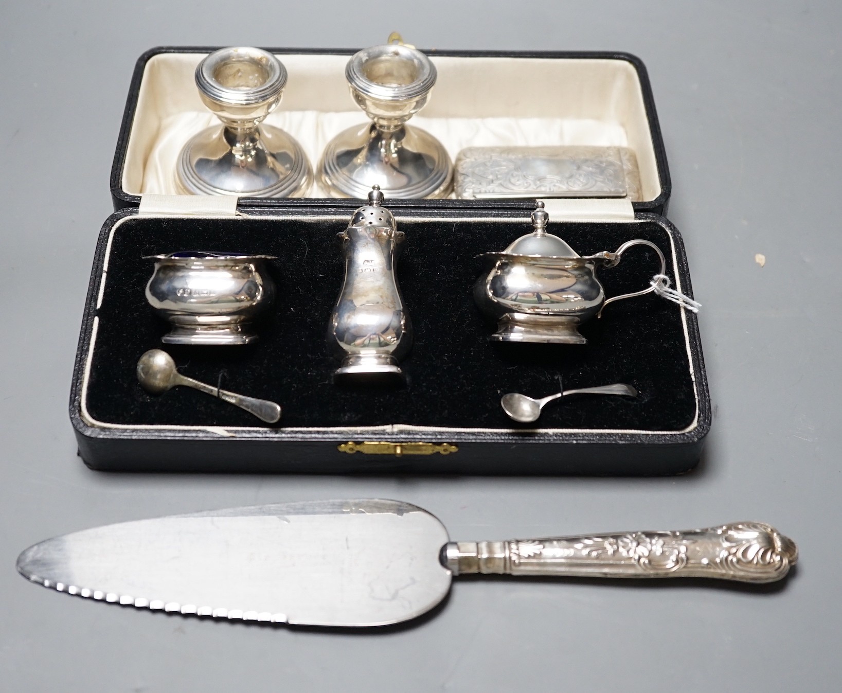 A cased George V silver three piece condiment set, Birmingham, 1930, a Victorian engraved silver snuff box, a pair of silver mounted dwarf candlesticks and a silver handled cake slice.